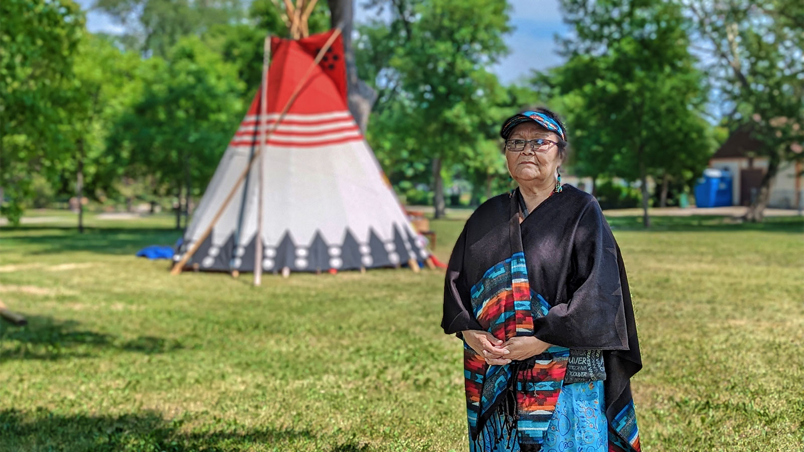 Lorraine stands outside in front of trees and a tepee