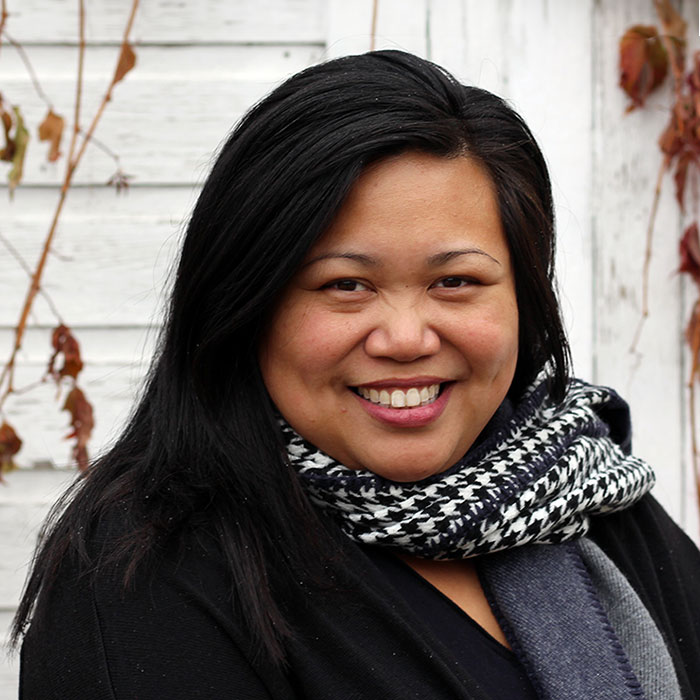 Millie Acuna smiling in front of wall with leafs and tree branches in background