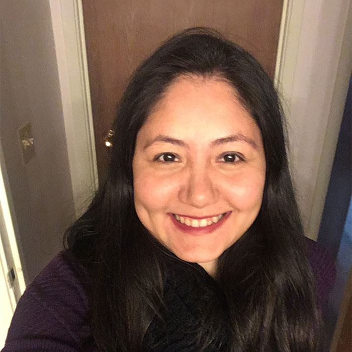 Roshani Perera smiling in a hallway with a closed door in the background