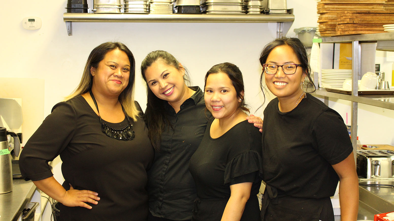 Four women smiling together in kitchen